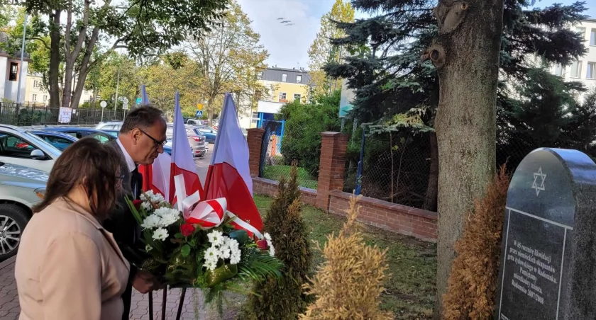 Na zdjęciu przedstawiciele miasta składają kwiaty pod macewą