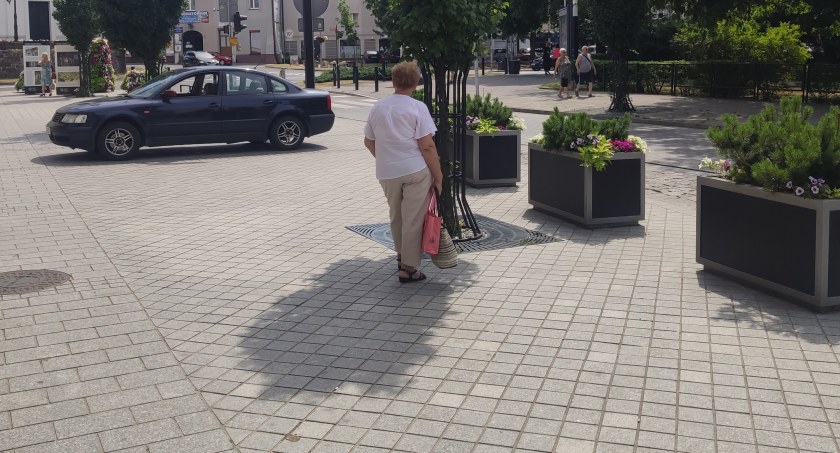 Na zdjęciu kobieta, która czeka na autobus, stanęła w cieniu kilka metrów od przystanku